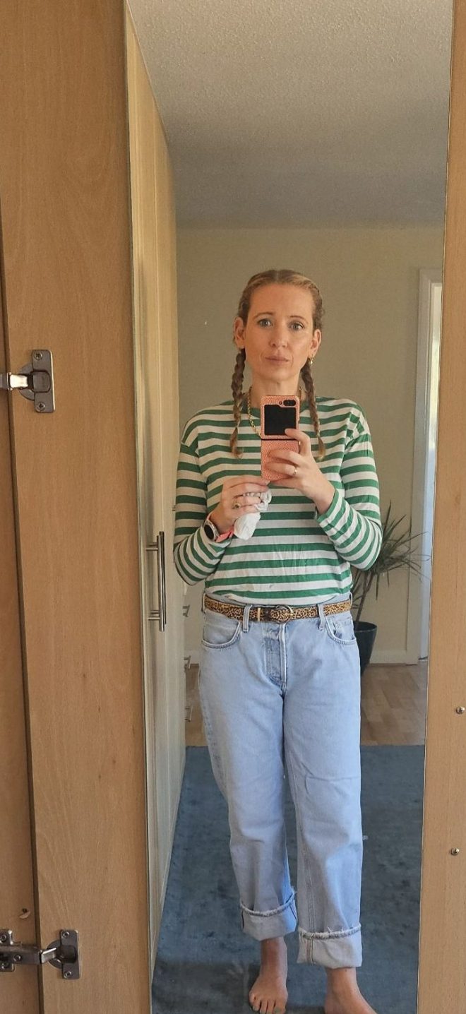 Woman with blonde hair in plaits wearing a striped long-sleeved t-shirt with jeans and leopard print belt.